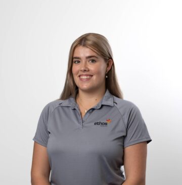Healthy young woman in grey Ethos Health polo shirt, smiling confidently.