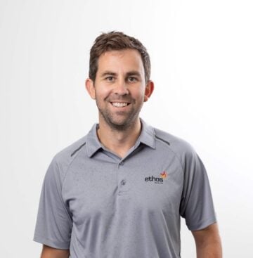 Friendly male healthcare professional smiling, wearing Ethos Health polo shirt, on white background.