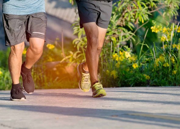 Close-up of two people jogging outdoors on a paved path surrounded by greenery and yellow flowers.