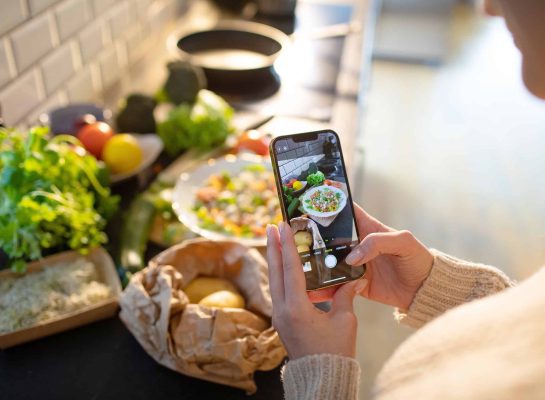 Woman in a cosy sweater taking a photo of a freshly prepared healthy meal with her smartphone in a kitchen.