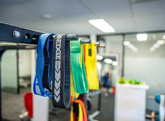 Close-up of colourful resistance bands hanging on a metal gym rack in a modern fitness facility.