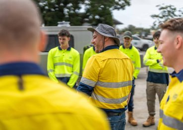 First aid training session outdoors with a group of young workers in high-visibility attire.